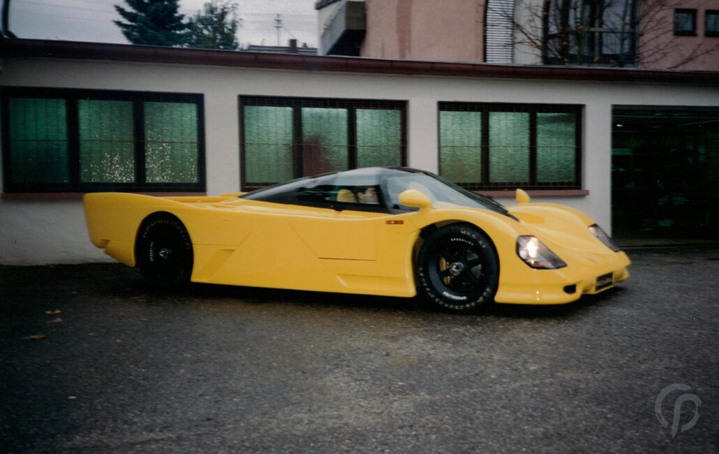 Dauer 962 gelb komplette Ansicht des Fahrzeugs Front und linke Seite mit geschlossenen Flügeltüren vor unserer Werkstatt mit 962 Le Mans Nummernschild