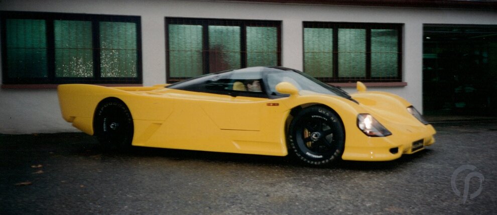 Dauer 962 gelb komplette Ansicht des Fahrzeugs Front und linke Seite mit geschlossenen Flügeltüren vor unserer Werkstatt mit 962 Le Mans Nummernschild